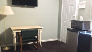 Una habitación con una televisión de pantalla plana en la pared, un escritorio con una silla, un refrigerador y una puerta.