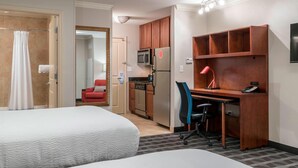 Ein Hotelzimmer mit zwei Betten, einer Küchenzeile, einem Schreibtisch mit Stuhl und einer roten Lampe.