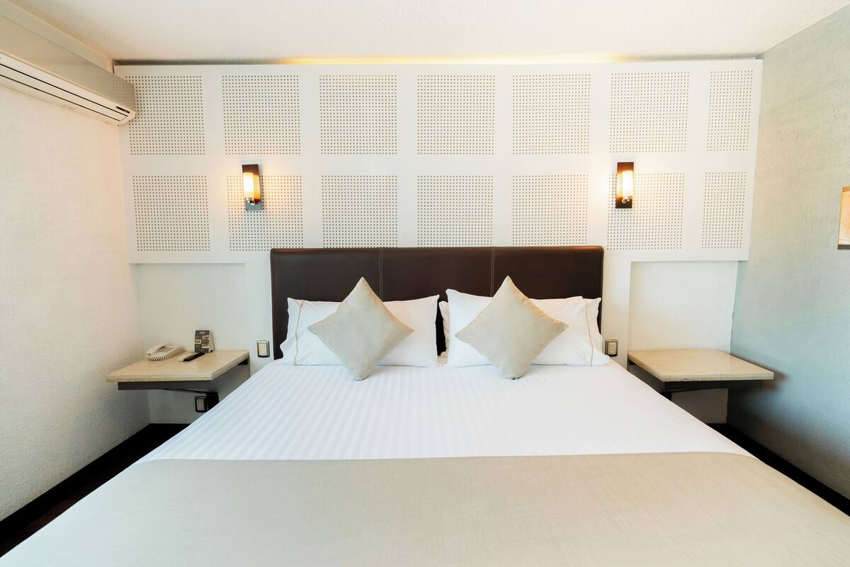 A hotel room with a large bed, two bedside tables, and a headboard with a perforated design.