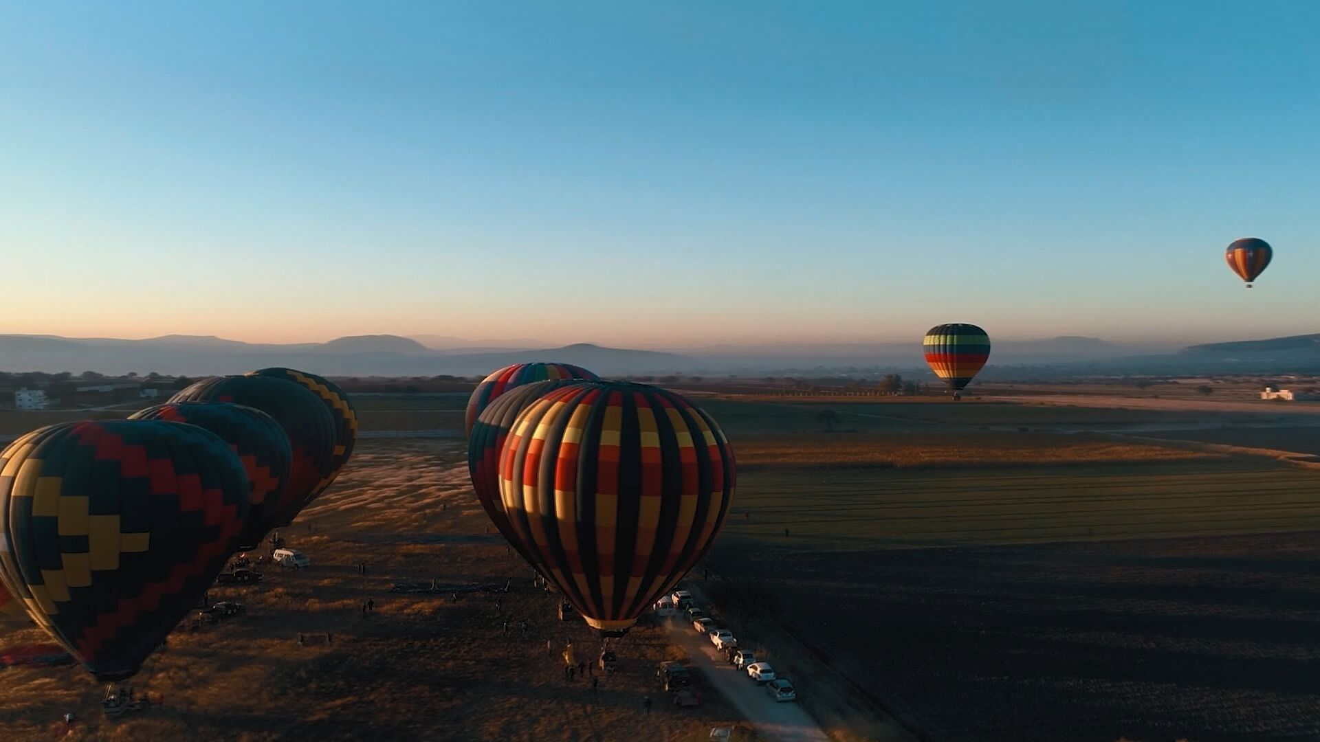 A row of hot air balloons parked on a dirt field with a clear sky in the background.