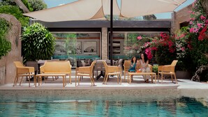 A poolside area with wicker chairs and tables, a glass enclosure with artwork, and lush greenery. - Hotel Rio Tequisquiapan (Tequisquiapan)