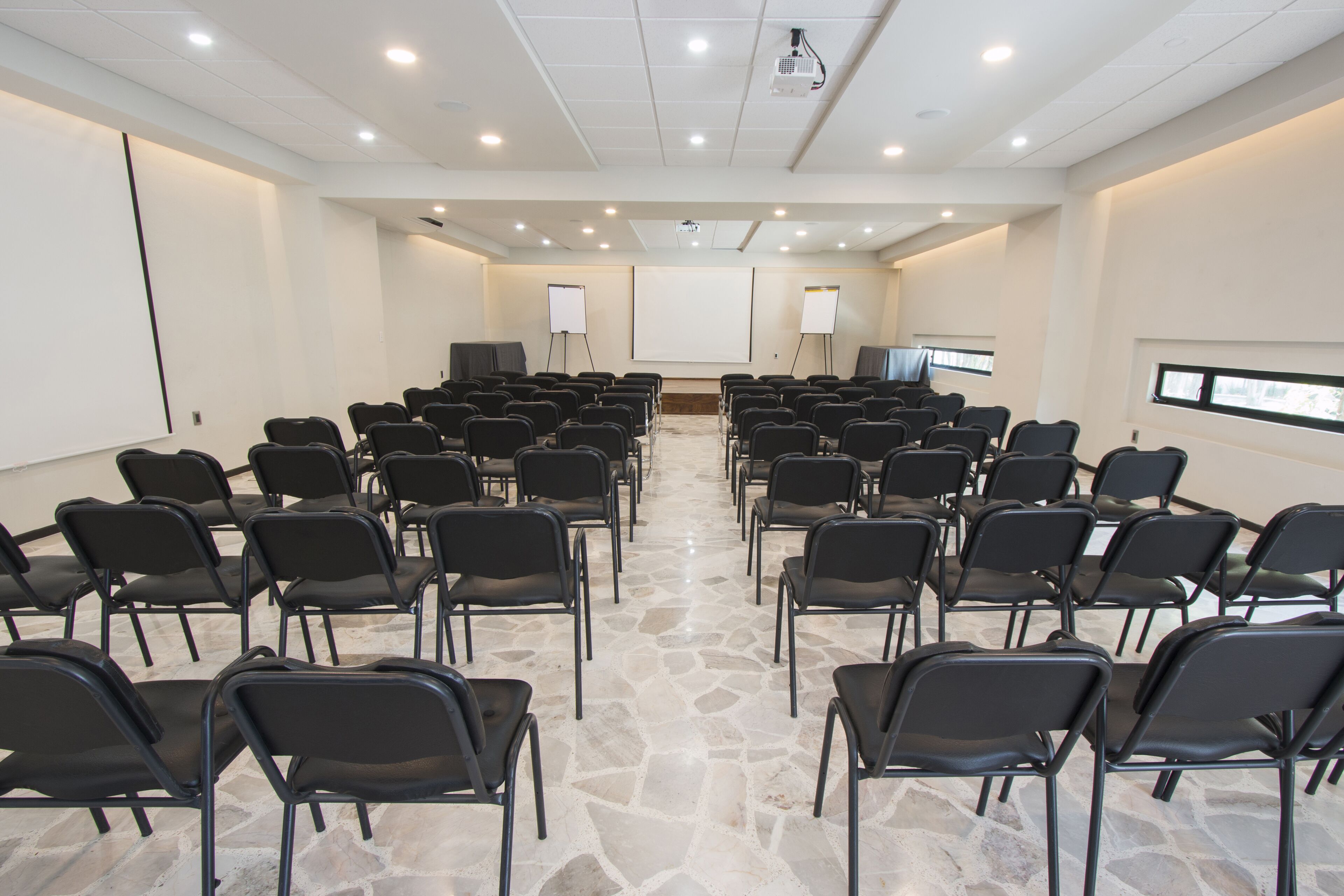 Un salón de conferencias con filas de sillas, un proyector y una pizarra.