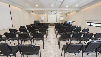 Un salón de conferencias con filas de sillas, un proyector y una pizarra.