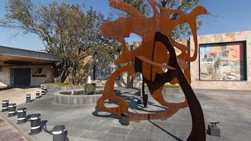 Een modern sculptuur in een openbare plein, met een stenen gebouw op de achtergrond.
