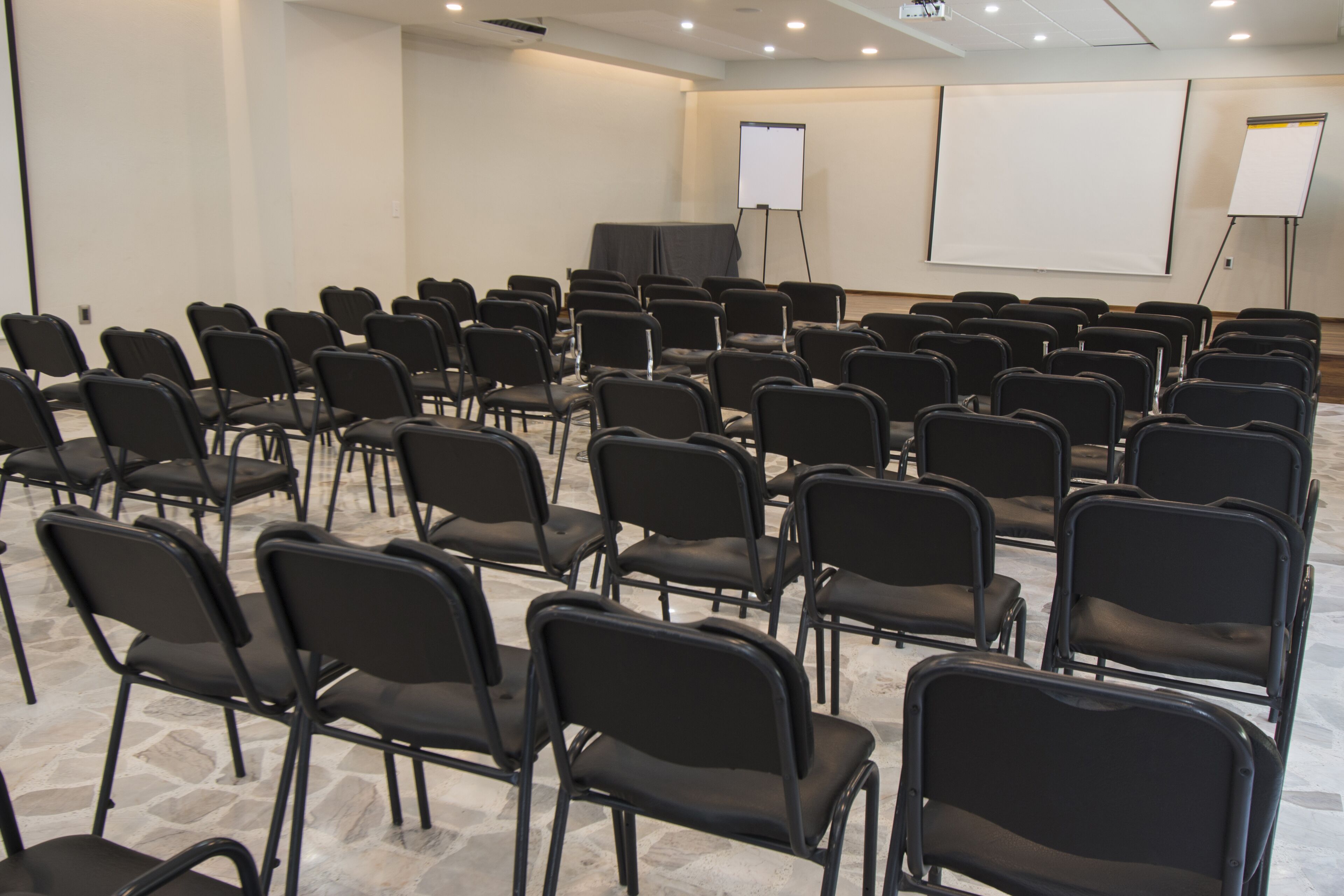 A conference room with rows of black chairs, a white projection screen, and a whiteboard.