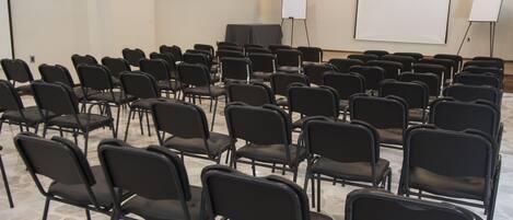 A conference room with rows of black chairs, a white projection screen, and a whiteboard.