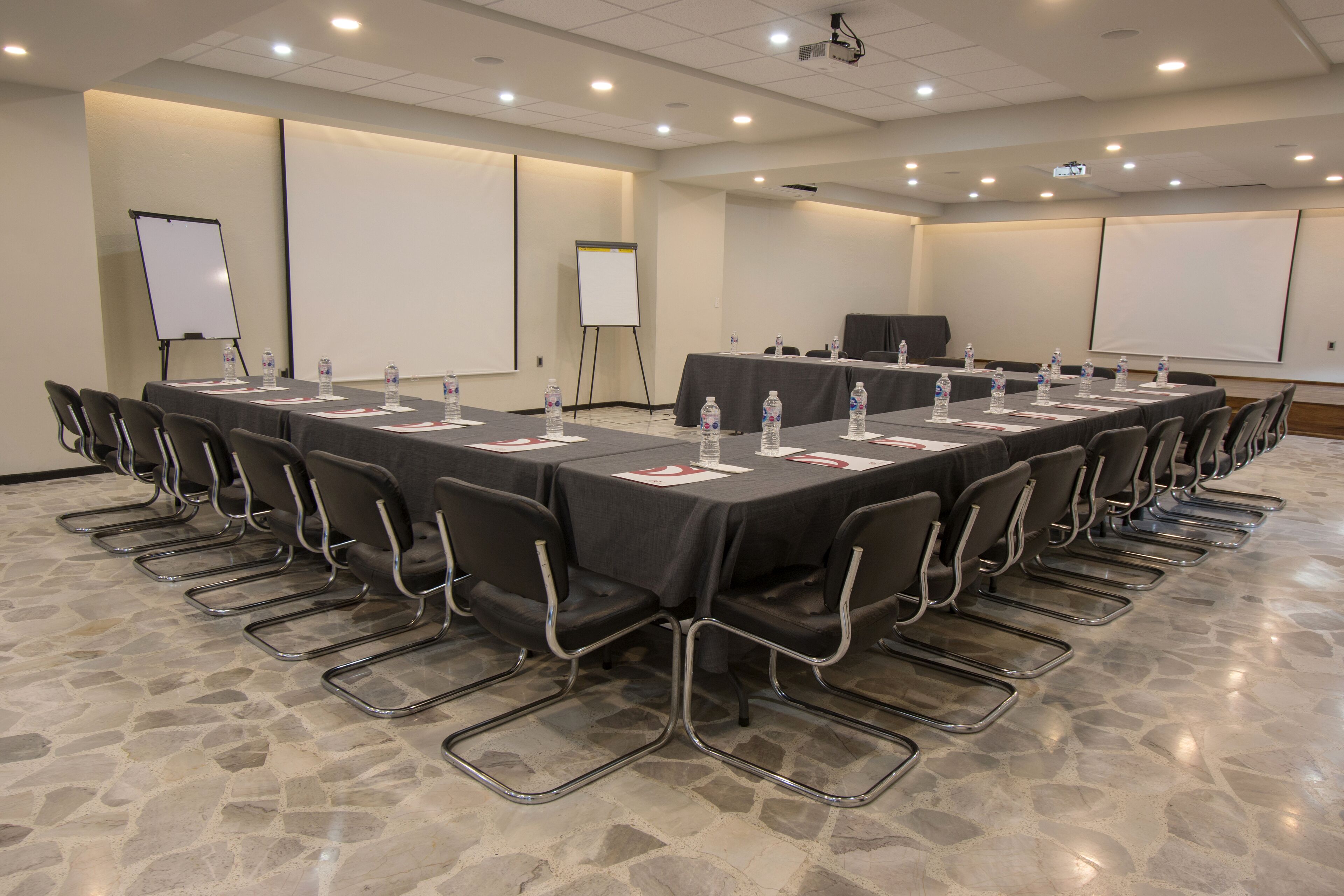 Un salón de conferencias con una larga mesa, sillas y una pantalla de proyector.