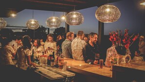 A crowded bar with hanging spherical chandeliers, a bar counter with various bottles and glasses, and a group of people socializing. - Hotel Rio Tequisquiapan (Tequisquiapan)
