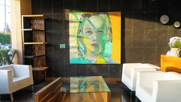 A modern lobby with a large abstract painting, white sofas, a glass coffee table, and a wooden bookshelf.