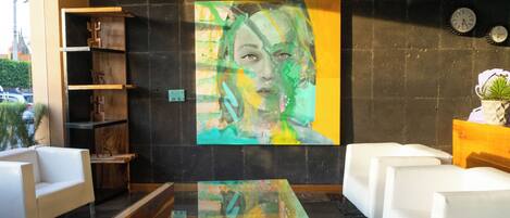 Un vestíbulo moderno con un cuadro abstracto grande, sofás blancos, una mesa de centro de cristal y una estantería de madera.