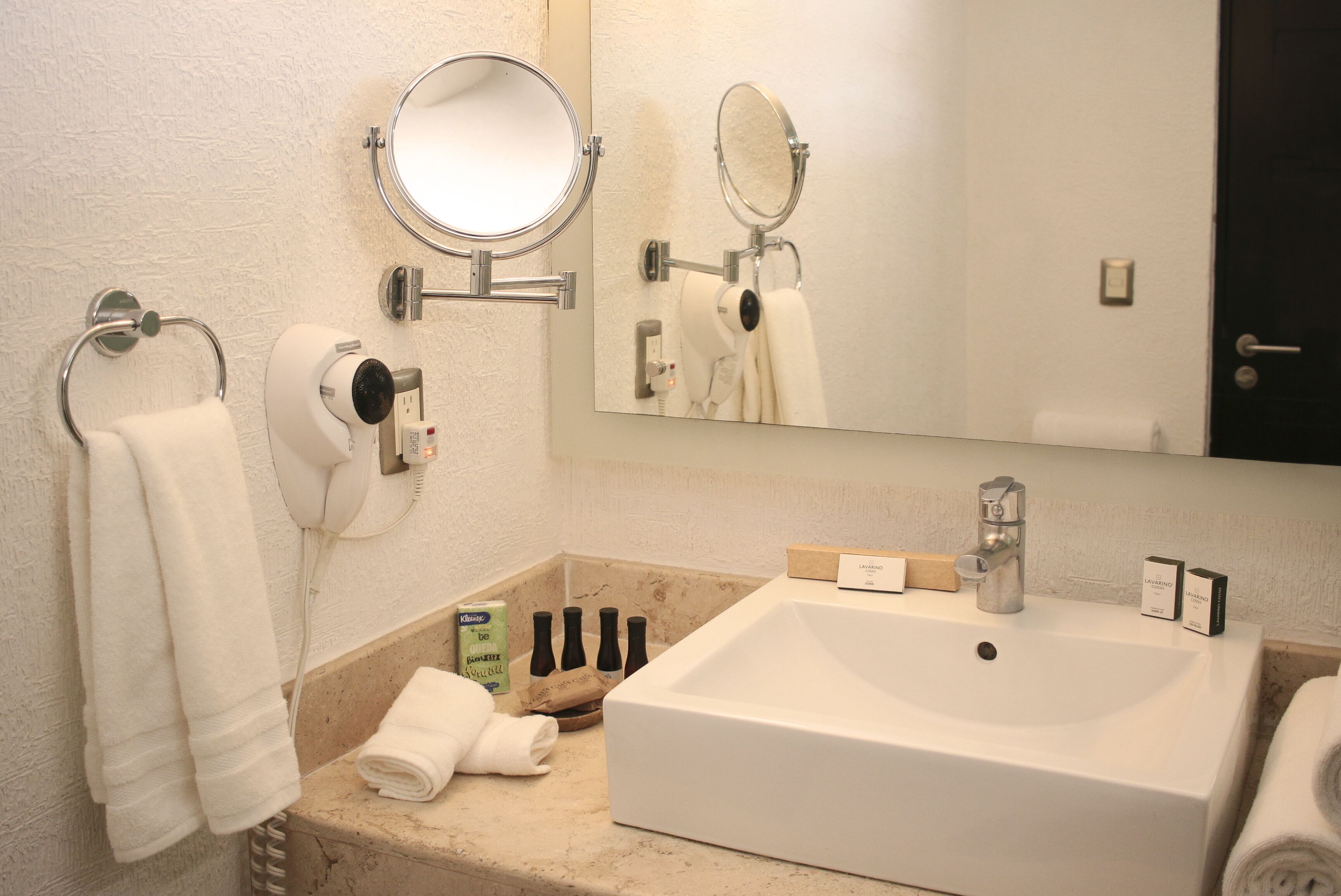 A bathroom with a white sink, a mirror, a towel rack, and a bottle of shampoo.