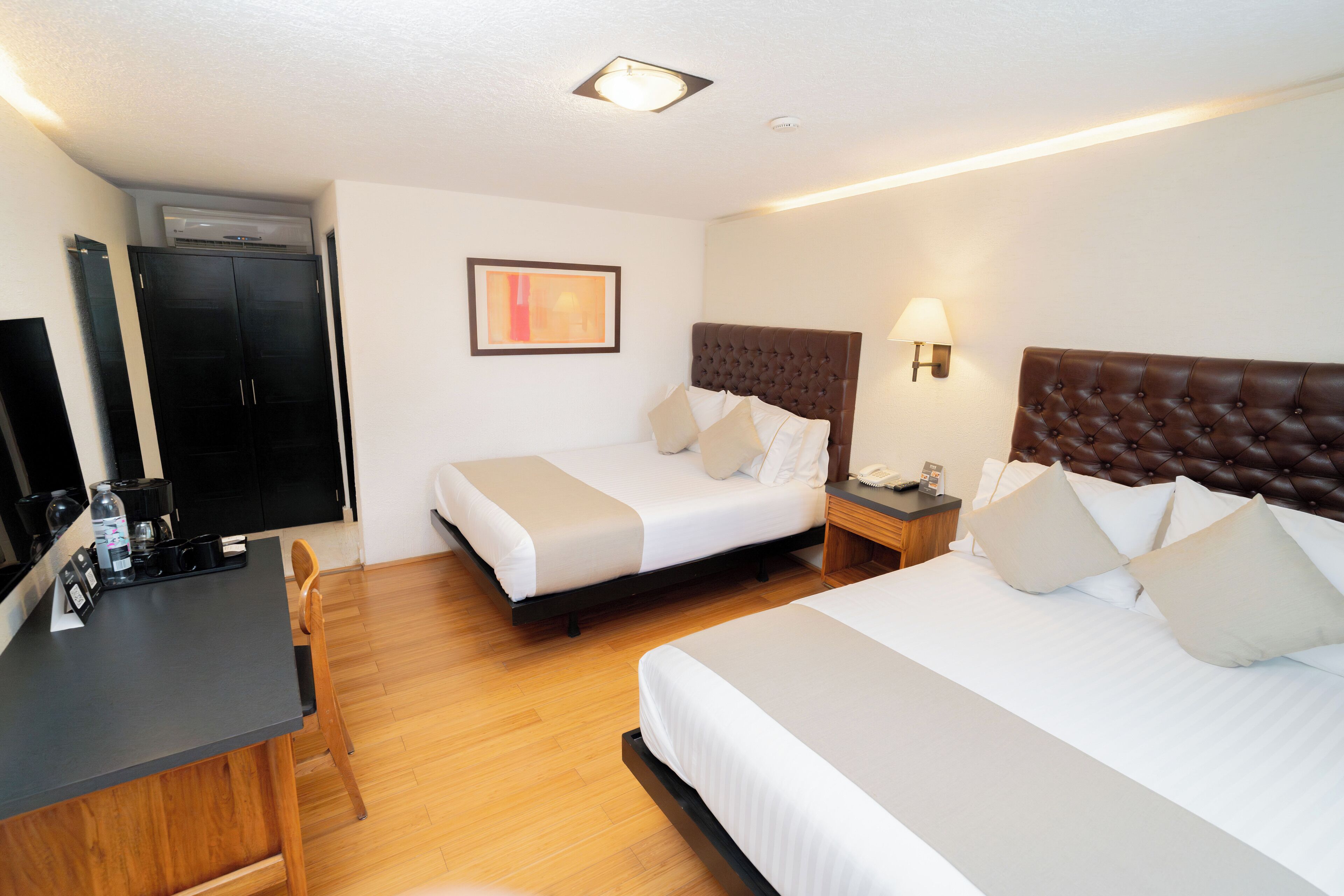 A hotel room with two beds, a desk, a chair, a wardrobe, and a wall-mounted TV.