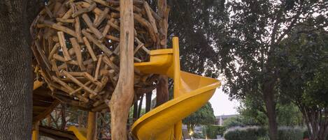 A playground with a yellow slide and a climbing structure made of logs.