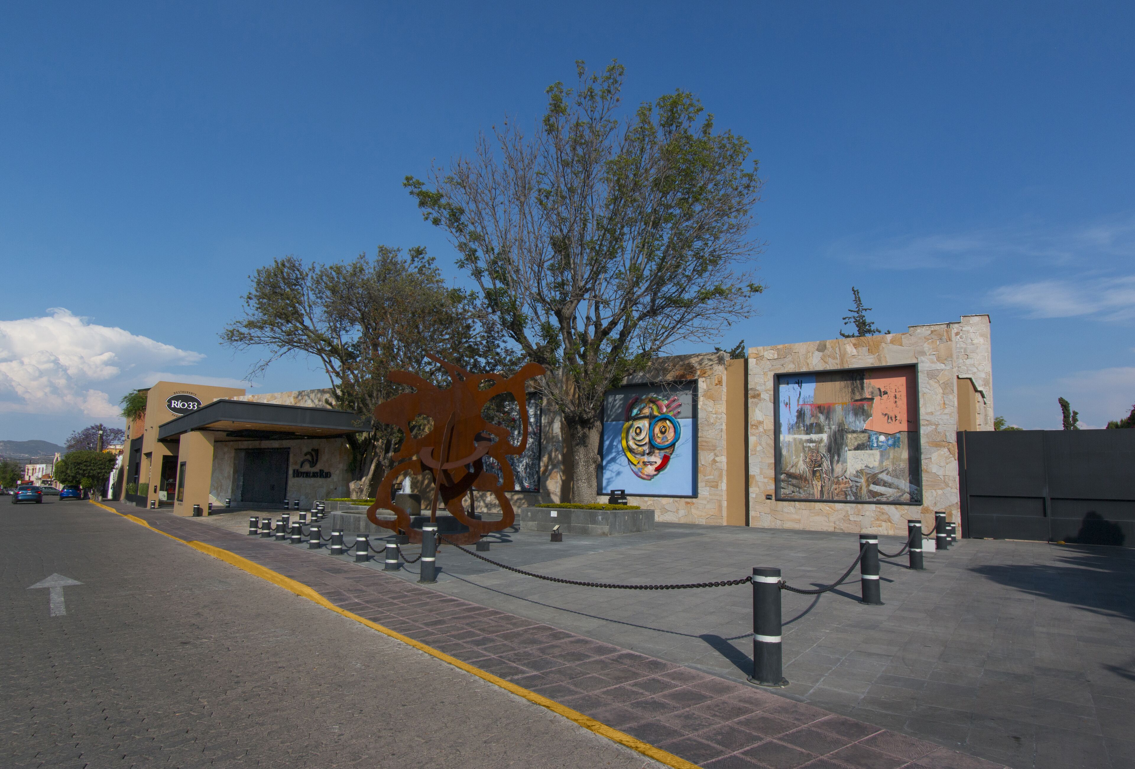 A building with a modern design, featuring a large tree in front, a metal sculpture, and a mural on the side.