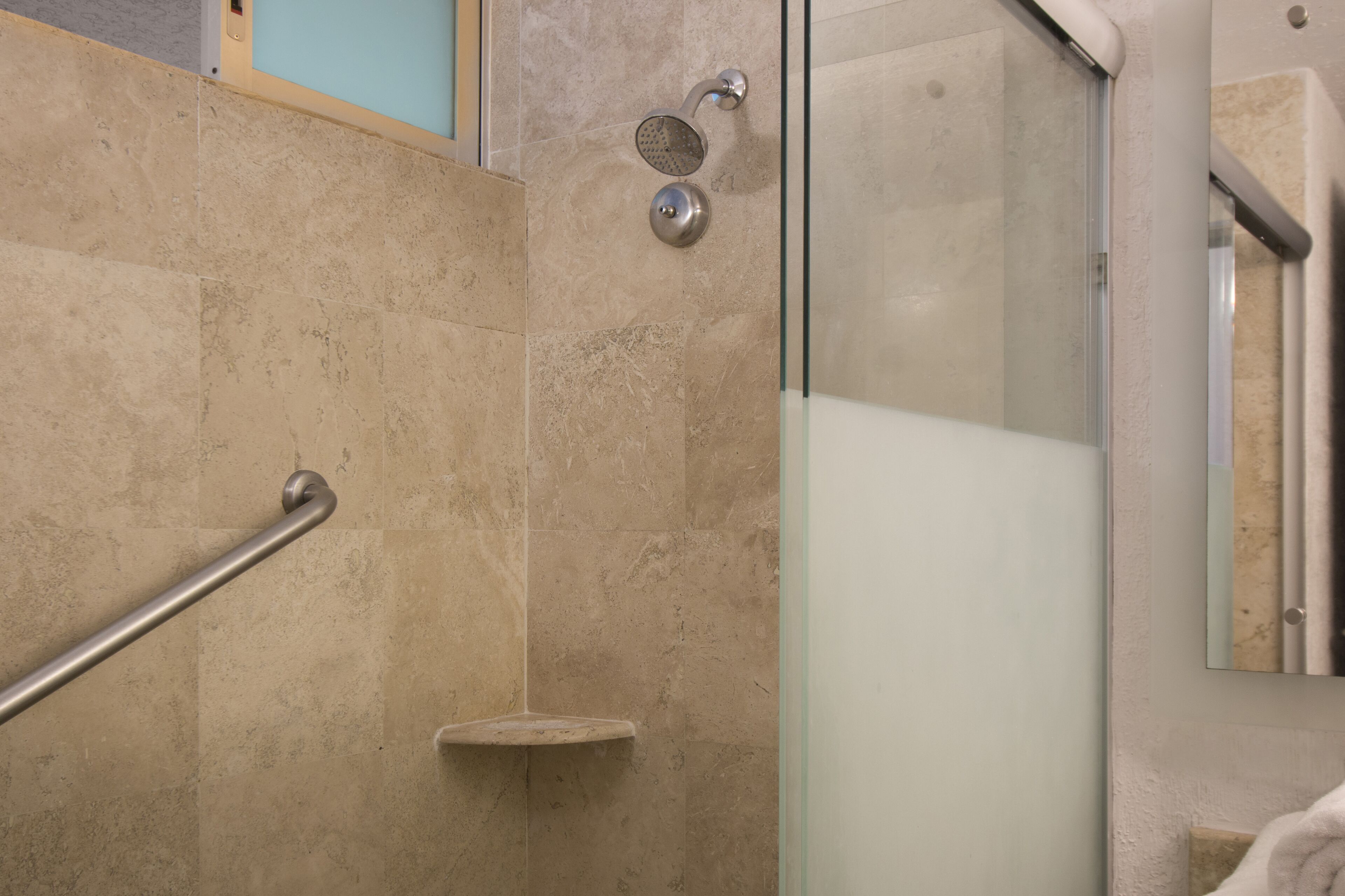 A glass-enclosed shower with a handheld showerhead and a handheld showerhead with a circular spray nozzle.