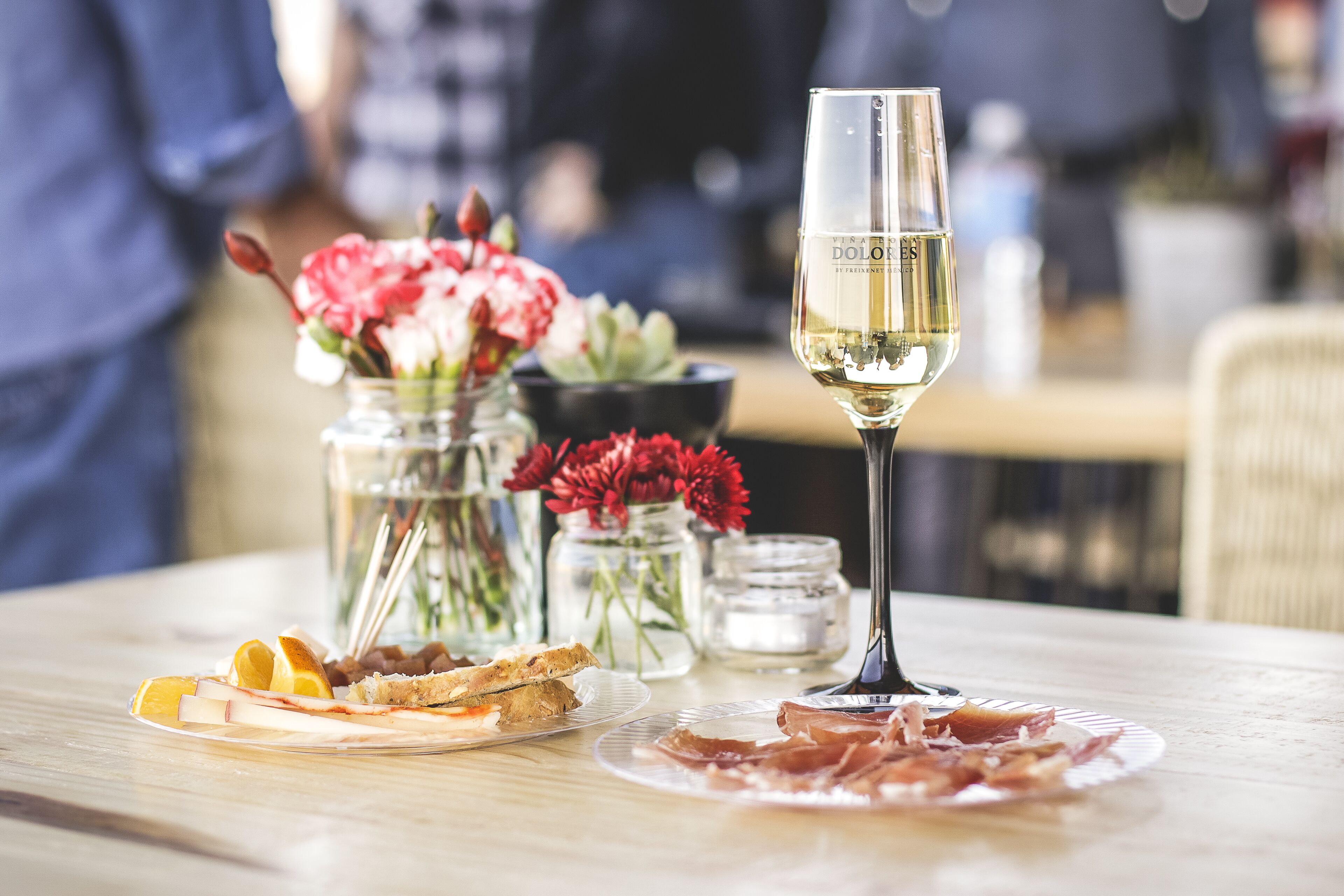 A dining table with plates of food, a glass of white wine, and decorative jars with flowers.