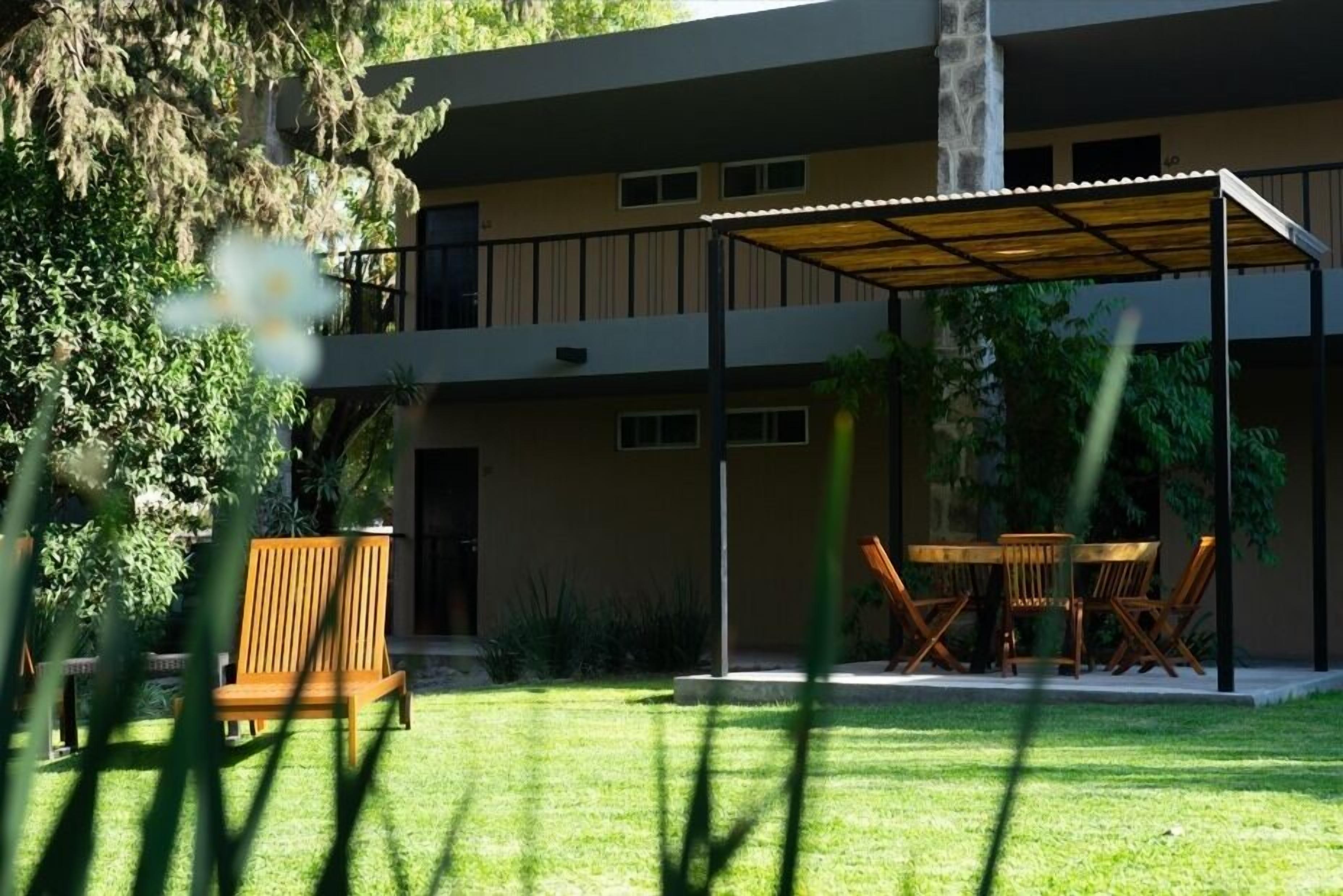 Un edificio de dos plantas con un patio cubierto, mobiliario exterior y un césped bien cuidado.