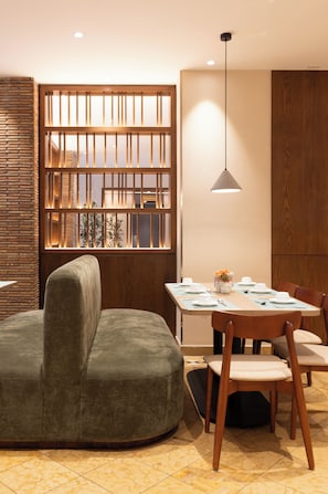 Un comedor con mesa de madera preparada para cuatro personas, un banco acolchado y una lámpara colgante.
