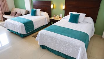 Habitación de hotel con dos camas, cada una con colcha azul turquesa y blanca, cabecero de madera y mesita de noche con teléfono y un libro.