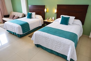 Habitación de hotel con dos camas, cada una con colcha azul turquesa y blanca, cabecero de madera y mesita de noche con teléfono y un libro.