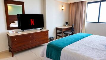 Habitació d'hotel amb llit, escriptori, televisió i finestra amb cortines.