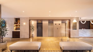 Een hotel lobby met een receptiebalie, een zithoek met twee comfortabele banken, een kamerplant en een lift.