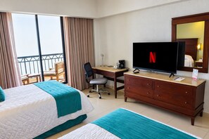 Habitación de hotel con dos camas, un escritorio, un televisor y un balcón con cortinas.
