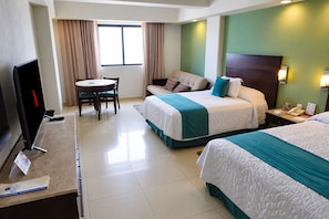 Quarto de hotel com duas camas, uma mesa de escritório com computador, televisão e área de refeições com mesa e cadeiras.