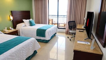A hotel room with two beds, a desk with a computer, a TV, and a balcony with a view.