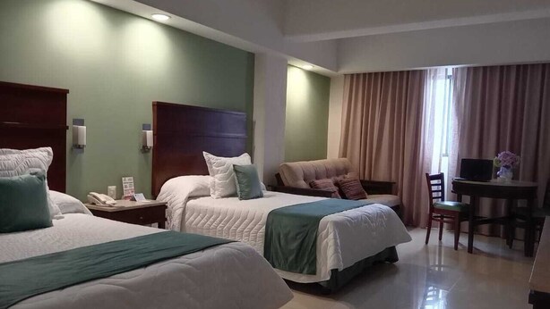 Habitación de hotel con dos camas, un escritorio, una silla y una ventana con cortinas.