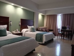Une chambre d’hôtel avec deux lits, un bureau, une chaise et une fenêtre avec des rideaux.