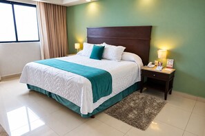 Una habitación de hotel con una cama grande, dos mesitas de noche con lámparas, una alfombra y una ventana con cortinas.