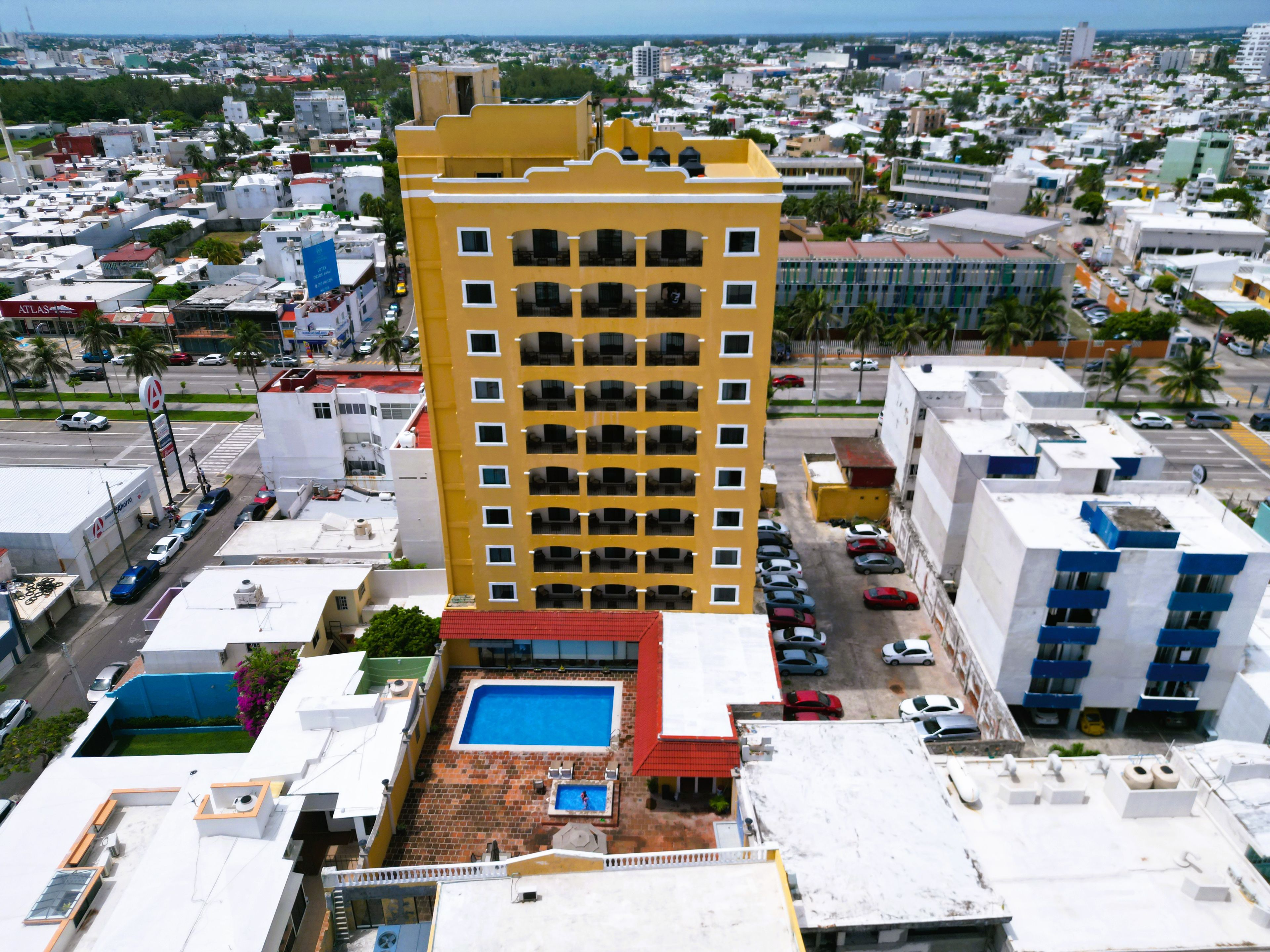 Un edificio de gran altura con varios balcones, piscina en la azotea y zona de estacionamiento.