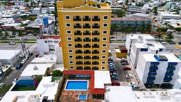 Un edificio de gran altura con varios balcones, piscina en la azotea y zona de estacionamiento.
