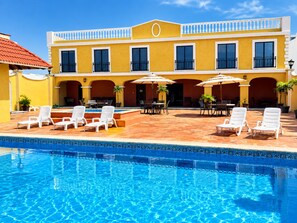 Un hotel con piscina, mobiliario exterior y fachada amarilla.