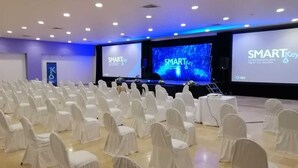 Un salón de conferencias con filas de sillas blancas, un escenario con una pantalla grande que muestra 'SMARTKey' y un logotipo en la pared.