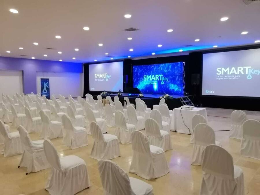A conference room with rows of white chairs, a stage with a large screen displaying 'SMARTKey,' and a logo on the wall.