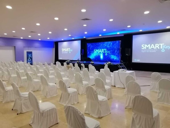 Un salón de conferencias con filas de sillas blancas, un escenario con una pantalla grande que muestra 'SMARTKey' y un logotipo en la pared.
