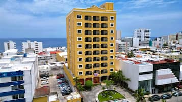 A high-rise hotel with multiple balconies, a parking lot, and a view of the ocean.