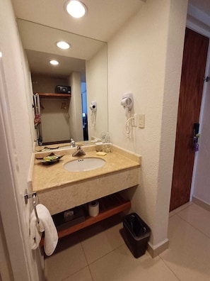 Une salle de bain équipée d’un lavabo, d’un miroir, d’un sèche-cheveux et d’un porte-serviettes.