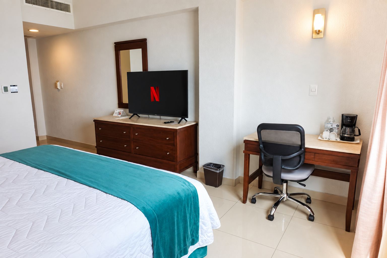 A hotel room with a bed, a desk, a chair, a television, and a coffee maker.