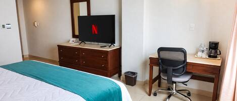 Una habitación de hotel con cama, escritorio, silla, televisor y cafetera.