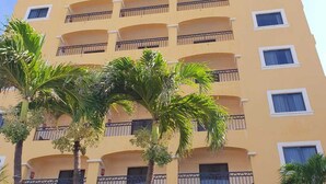 Un hotel de varios pisos con balcones, palmeras y una puerta roja.