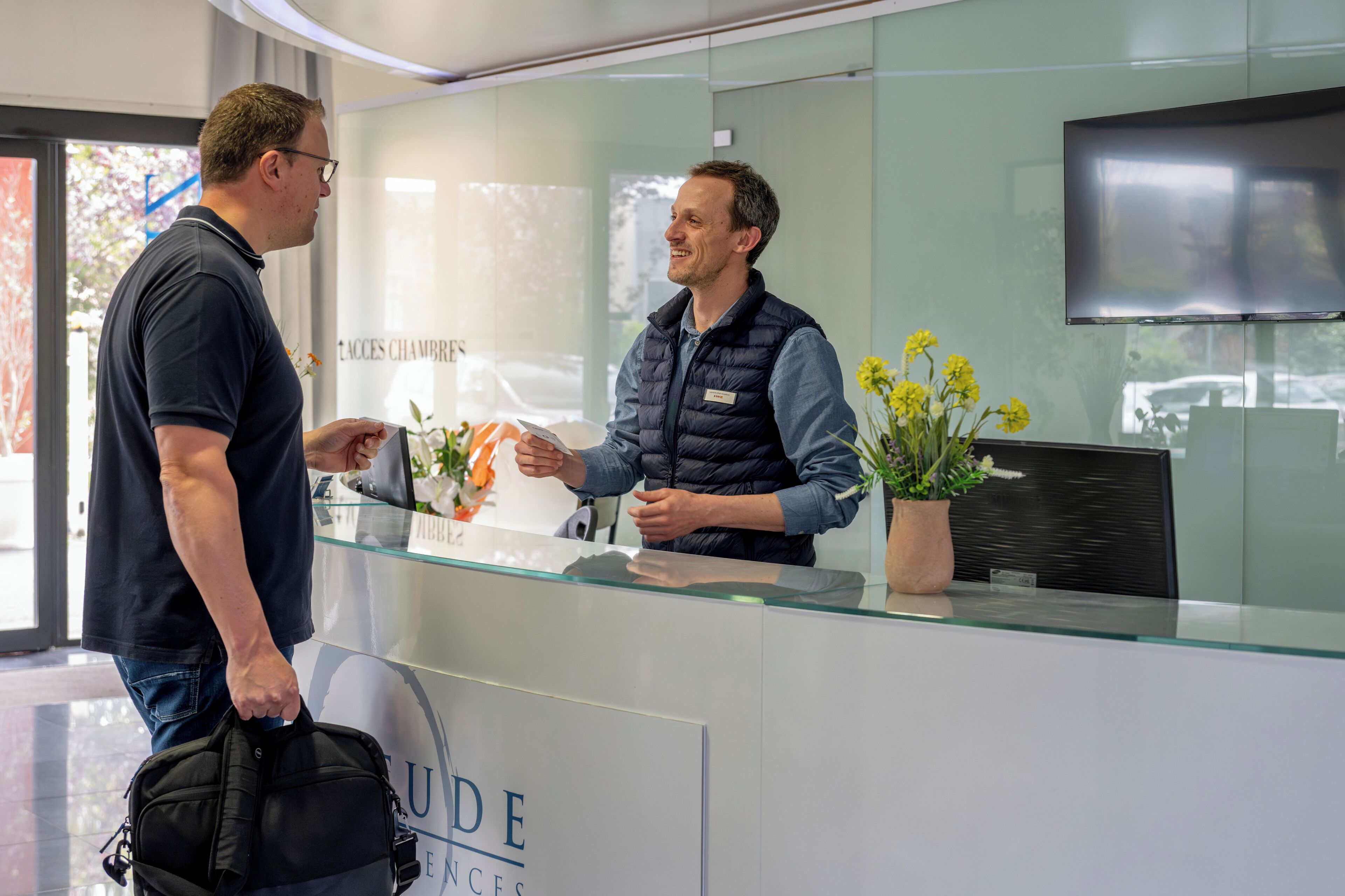 A reception area with a glass counter, a name tag, and a potted plant with yellow flowers.