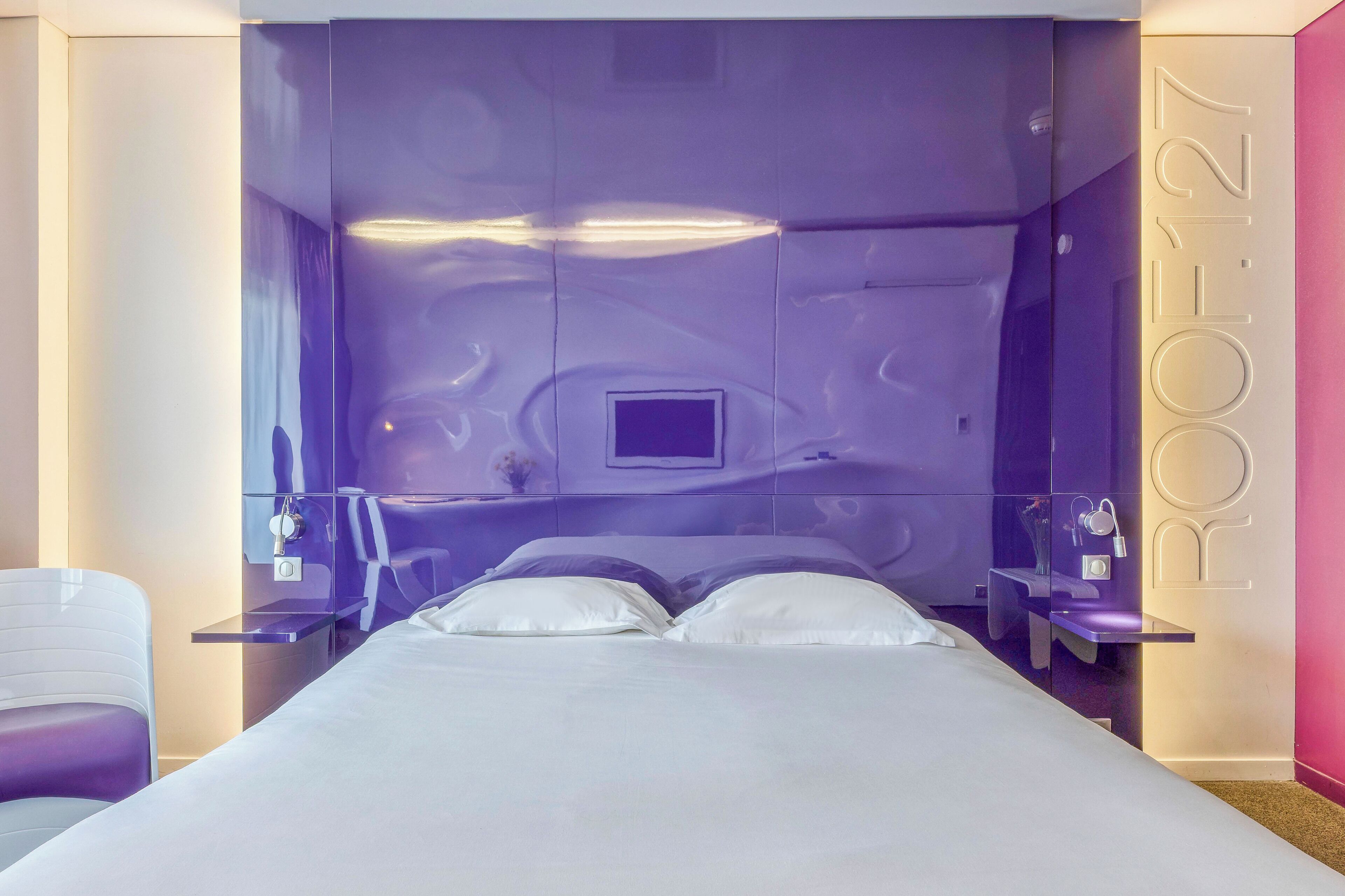 Una habitación de hotel moderna con una cama grande, dos mesitas de noche y un televisor integrado.