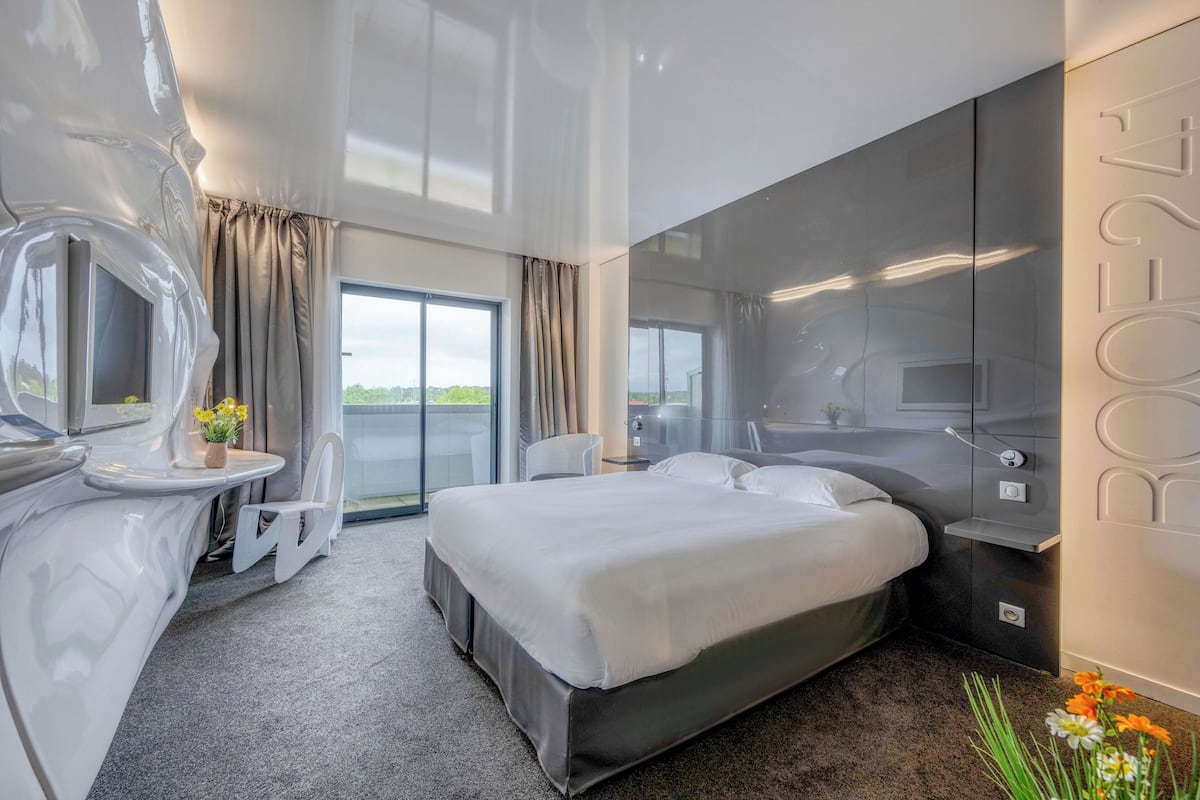 Une chambre d’hôtel moderne avec un grand lit, une salle de bain avec un miroir et une vue sur l’extérieur.