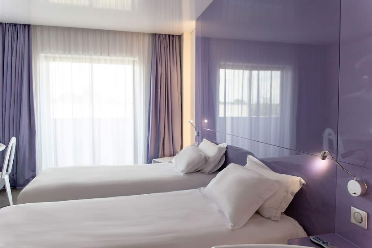 Une chambre d’hôtel avec deux lits, un miroir, une table de chevet et une fenêtre avec des rideaux.