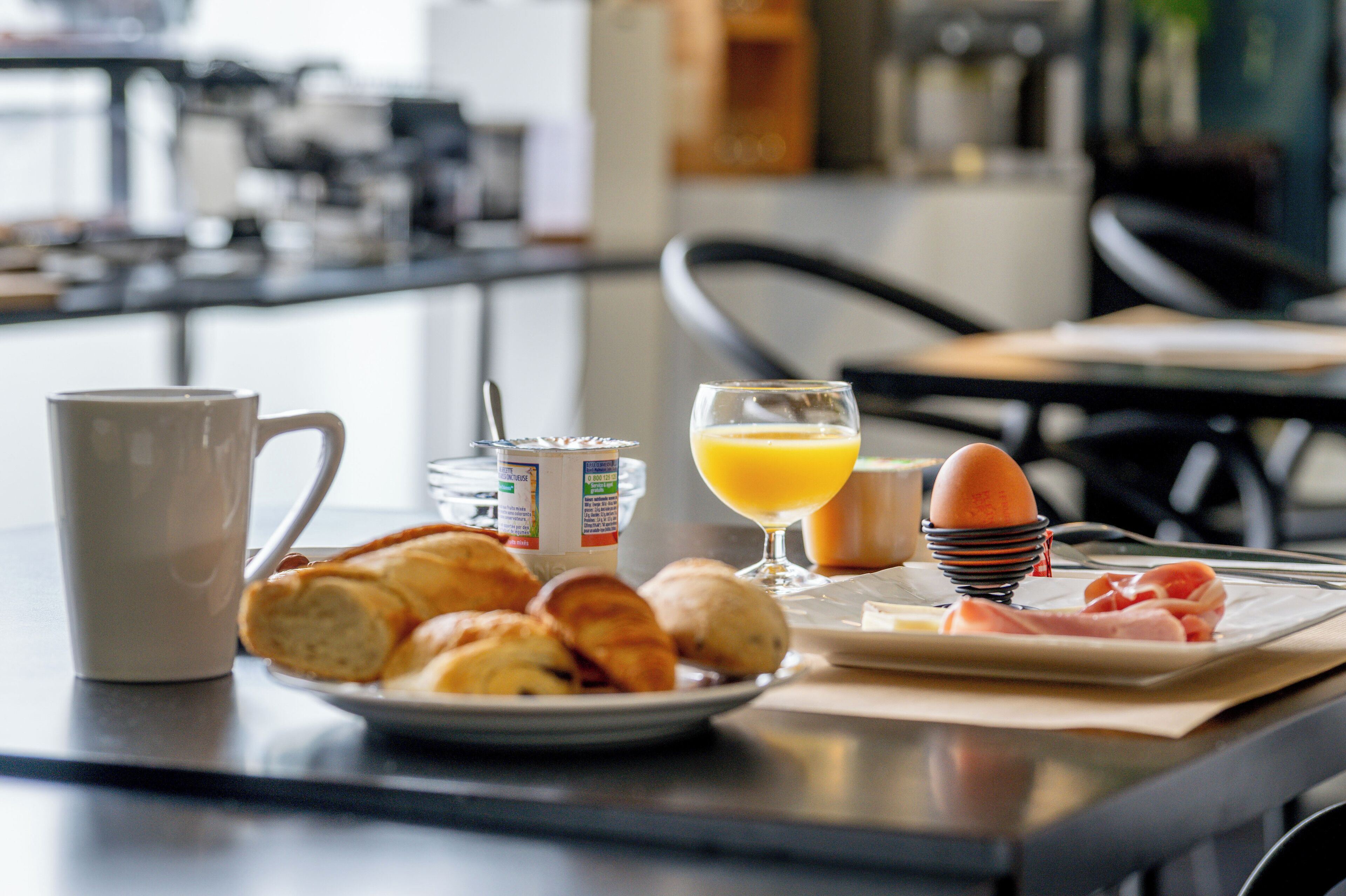 Ein Frühstückstisch mit Croissants, einem Glas Orangensaft, einer Kaffeetasse und einem Teller mit Schinken und Eiern.