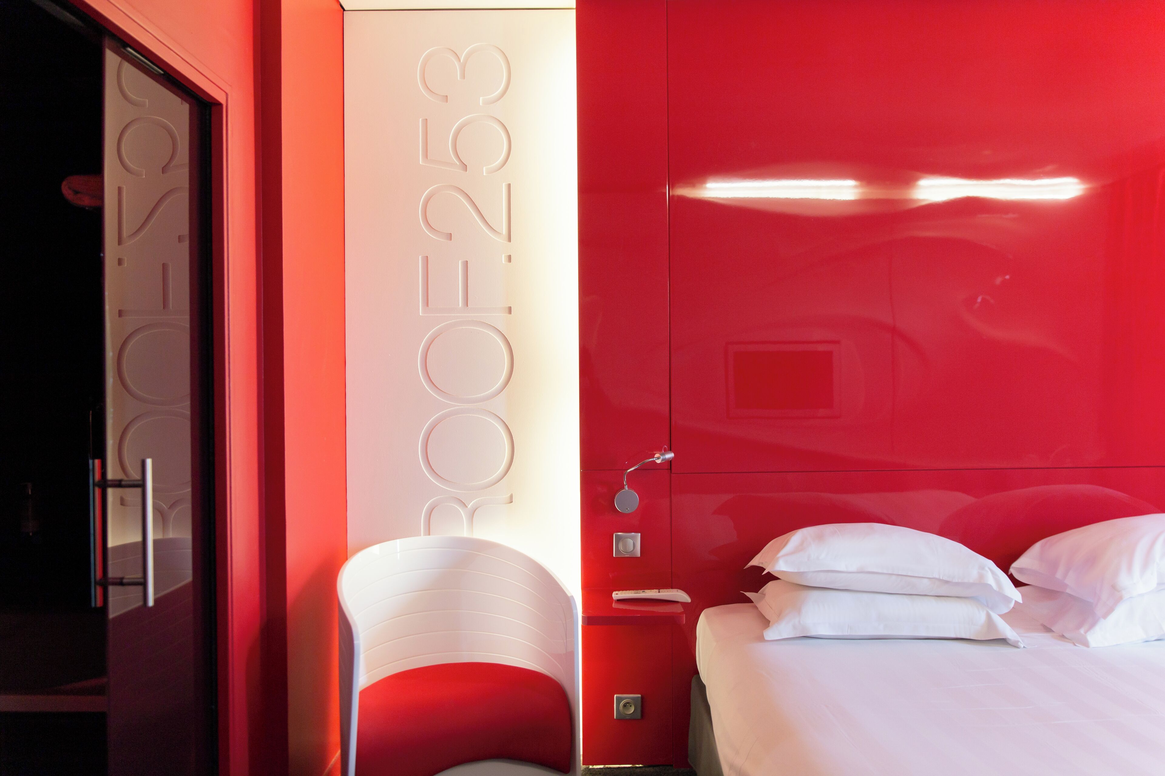 Ein Hotelzimmer mit roter Wand, einem Bett mit weißer Bettwäsche und einem Nachttisch mit Lampe.