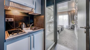 A modern kitchen with a built-in stove and a coffee maker, a glass door leading to a bedroom with a bed and a small table. - Comfort Aparthotel Bassin d'Arcachon (La Teste-de-Buch)